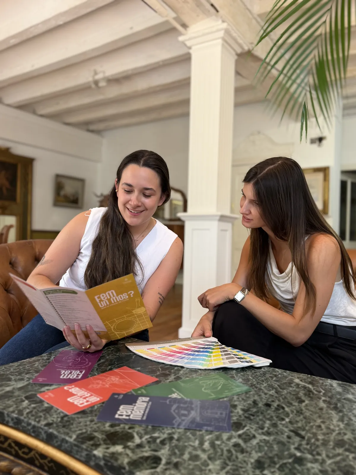 Diseñadoras de Paddock Comunicación revisando piezas impresas y una guía de color Pantone